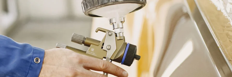Representative photo: technician using a spray gun on a masked car panel